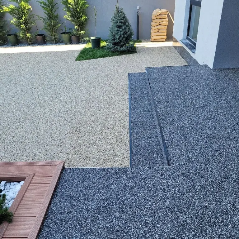 Curte cu covor de piatră crem și trepte antracit, lângă un deck de lemn cu plante