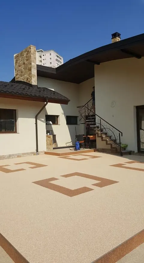 Terasă crem cu intarsii geometrice maro din covor de piatră, lângă o scară în spirală