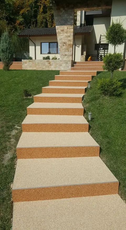 Trepte crem cu margini teracotă șerpuind prin gazonul unei grădini în pantă