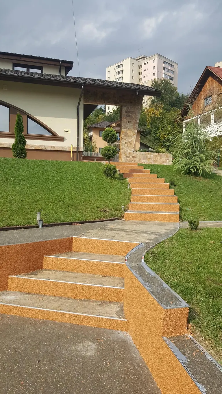 Trepte curbate din covor de piatră teracotă, coborând printr-o grădină cu gazon verde